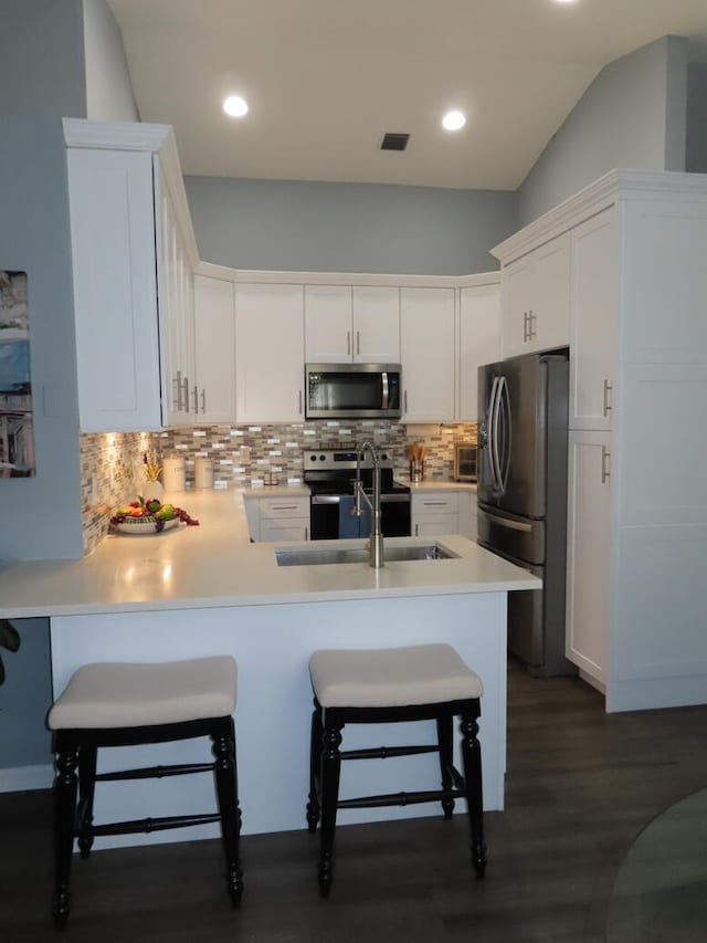 kitchen with white cabinets, kitchen peninsula, stainless steel appliances, a breakfast bar area, and decorative backsplash