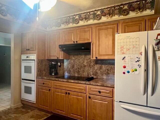 kitchen with decorative backsplash, white appliances, and dark stone countertops