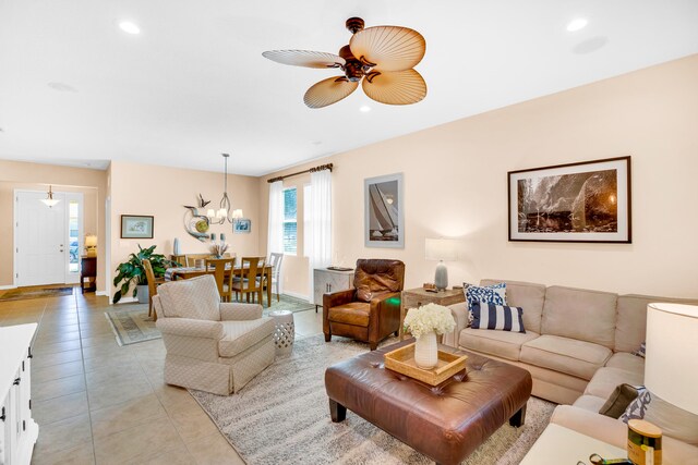 tiled living room with ceiling fan with notable chandelier