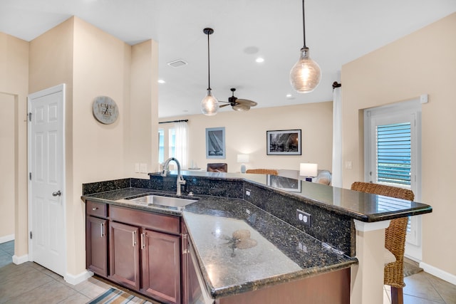 kitchen with dark stone countertops, light tile patterned floors, decorative light fixtures, and sink