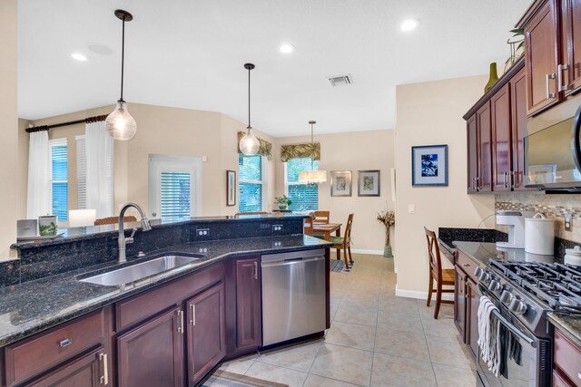 kitchen with dark stone countertops, appliances with stainless steel finishes, hanging light fixtures, and sink