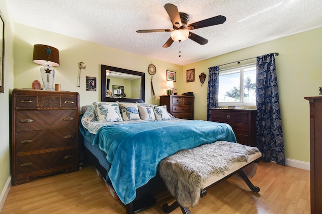 bedroom with light wood-type flooring, ceiling fan, and a textured ceiling