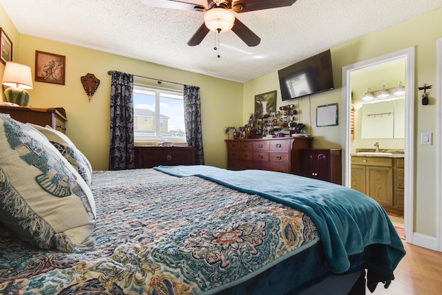 bedroom featuring light wood-type flooring, a textured ceiling, ceiling fan, ensuite bath, and sink