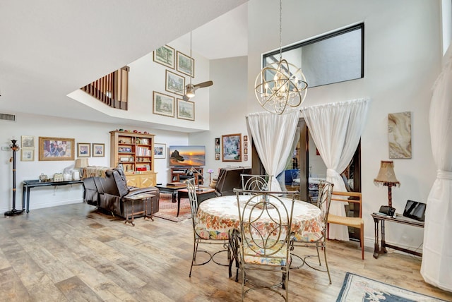 dining space with wood-type flooring, ceiling fan with notable chandelier, and a high ceiling