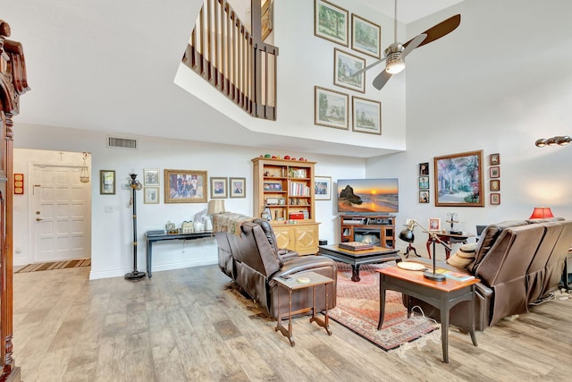 living room with a towering ceiling, light hardwood / wood-style floors, and ceiling fan