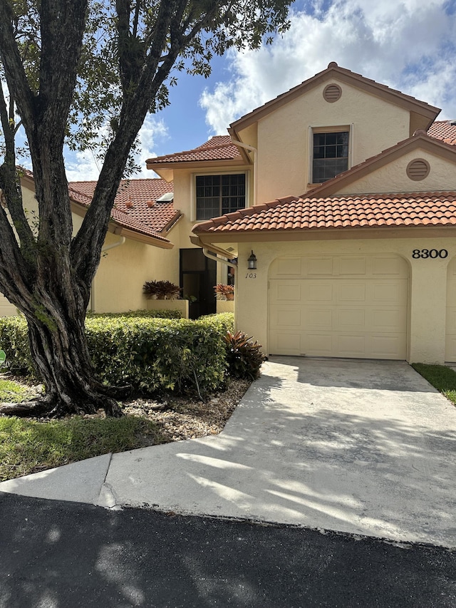 mediterranean / spanish-style home with an attached garage, stucco siding, a tiled roof, and concrete driveway