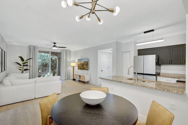 dining room featuring ceiling fan with notable chandelier, sink, light wood-type flooring, and ornamental molding