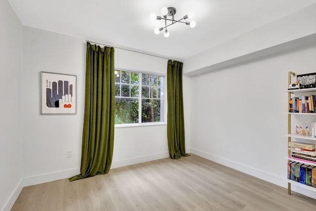 spare room with a notable chandelier and light wood-type flooring