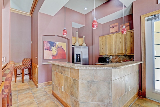 kitchen with hanging light fixtures, stainless steel fridge, tasteful backsplash, a high ceiling, and crown molding