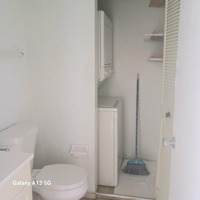 bathroom featuring stacked washing maching and dryer, vanity, and toilet