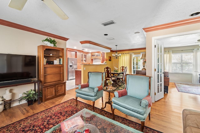 living room with a textured ceiling, ceiling fan with notable chandelier, light hardwood / wood-style floors, and ornamental molding