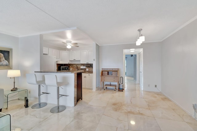 kitchen with white cabinets, backsplash, kitchen peninsula, and crown molding