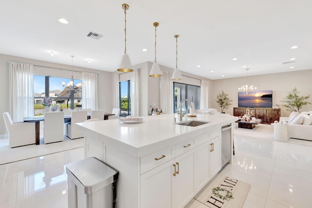 kitchen with white cabinets, a kitchen island with sink, a notable chandelier, decorative light fixtures, and sink