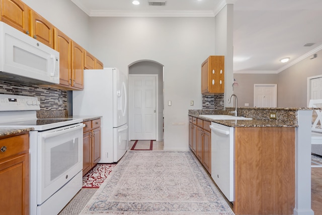 kitchen with dark stone counters, sink, kitchen peninsula, white appliances, and ornamental molding