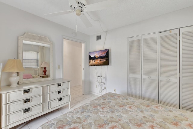 unfurnished bedroom with a textured ceiling, a closet, light tile patterned floors, and ceiling fan