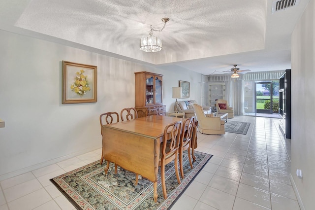 dining space featuring ceiling fan with notable chandelier, light tile patterned flooring, a raised ceiling, and a textured ceiling