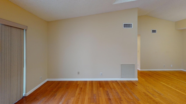 spare room featuring lofted ceiling, wood-type flooring, and a textured ceiling