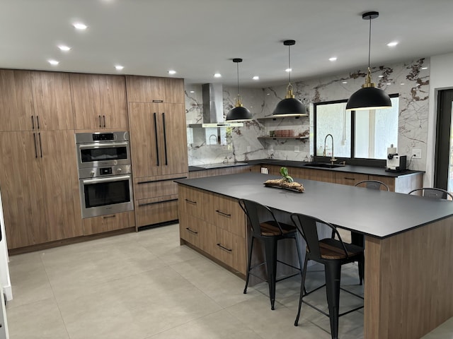 kitchen with stainless steel double oven, a kitchen bar, decorative light fixtures, sink, and a spacious island