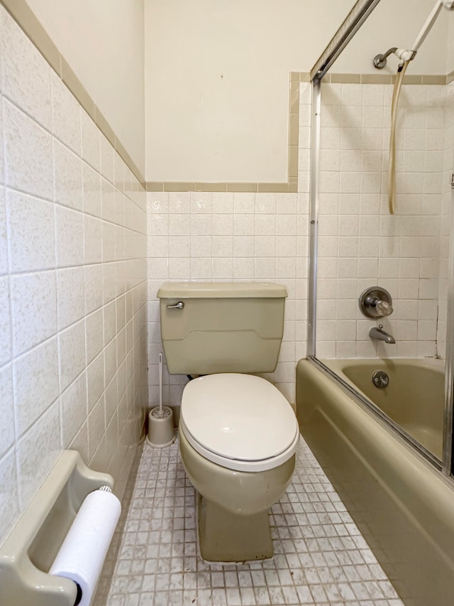 bathroom with tile walls, shower / bath combination with glass door, and toilet