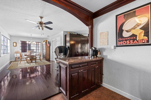 bar with dark stone countertops, ceiling fan with notable chandelier, pendant lighting, a textured ceiling, and hardwood / wood-style floors