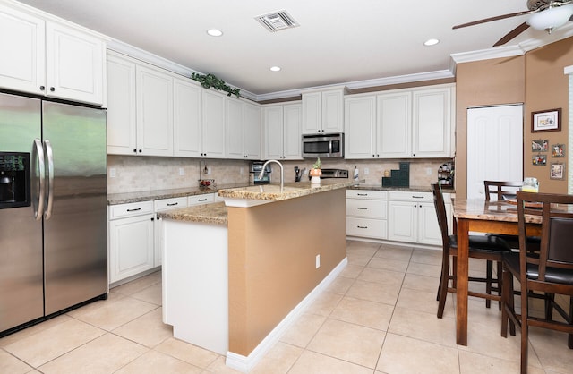 kitchen with a center island with sink, stainless steel appliances, ornamental molding, and white cabinetry