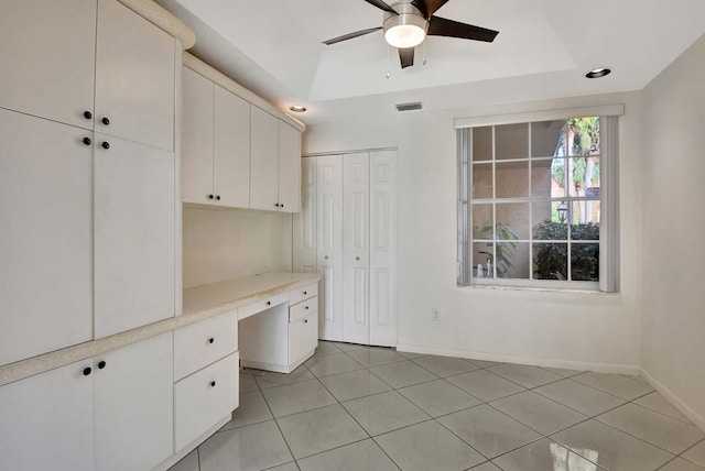 unfurnished office featuring light tile patterned floors, built in desk, a raised ceiling, and ceiling fan