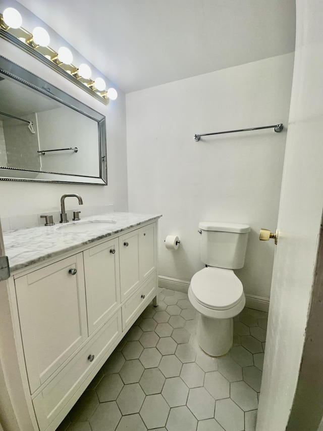 bathroom with toilet, tile patterned floors, baseboards, and vanity