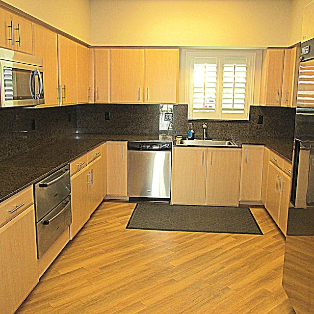 kitchen with decorative backsplash, stainless steel appliances, light brown cabinetry, light wood-type flooring, and a sink