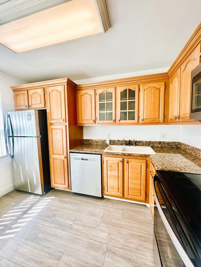 kitchen with dark stone counters, appliances with stainless steel finishes, a sink, and glass insert cabinets