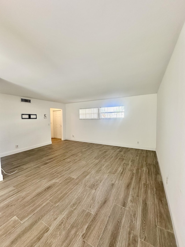 empty room with wood finished floors, visible vents, and baseboards