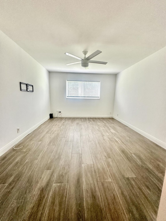 empty room with wood finished floors, a ceiling fan, and baseboards