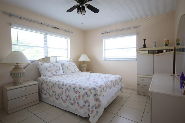 bedroom featuring ceiling fan, multiple windows, light tile patterned floors, and a textured ceiling