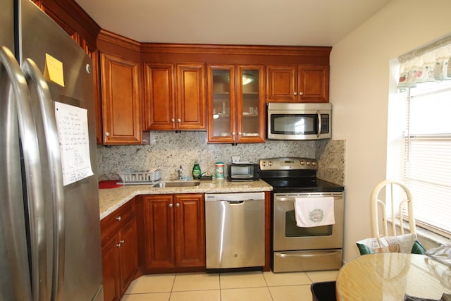 kitchen with sink, light tile patterned floors, backsplash, appliances with stainless steel finishes, and light stone countertops