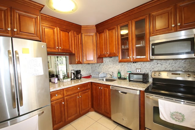 kitchen featuring light tile patterned floors, stainless steel appliances, sink, and light stone countertops