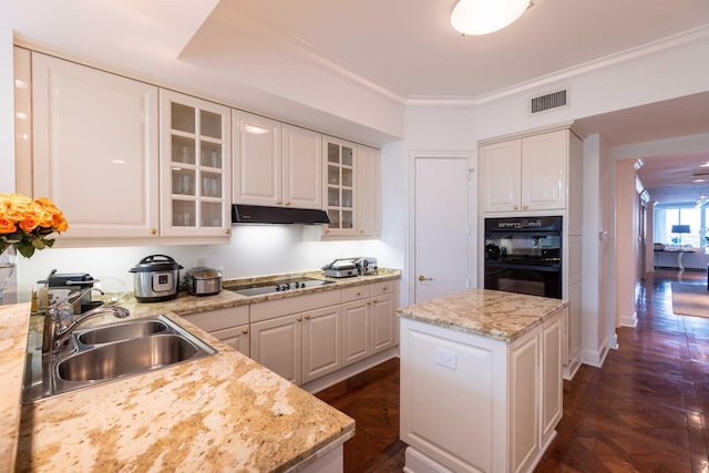 kitchen featuring white cabinets, a kitchen island, light stone countertops, sink, and stovetop