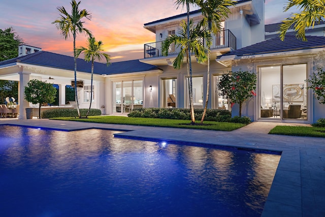 pool at dusk with ceiling fan, an outdoor pool, and a patio