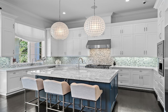 kitchen with white cabinets, wall chimney range hood, and an island with sink