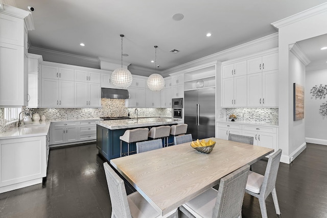 kitchen featuring built in appliances, white cabinetry, a center island with sink, and wall chimney exhaust hood