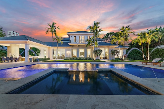 pool at dusk with pool water feature and a patio