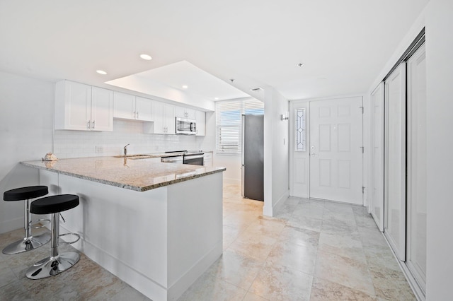 kitchen featuring kitchen peninsula, decorative backsplash, white cabinets, light stone counters, and stainless steel appliances