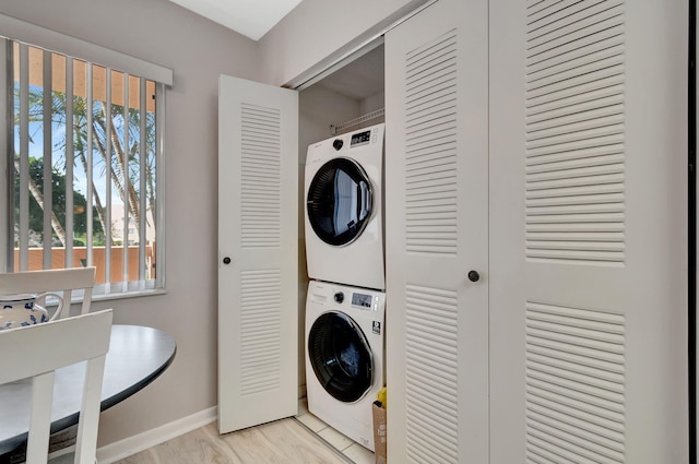 laundry area featuring stacked washer / drying machine, light wood-type flooring, and a wealth of natural light