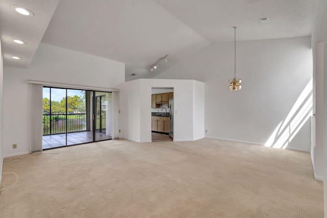 unfurnished living room featuring sink, track lighting, light colored carpet, and high vaulted ceiling