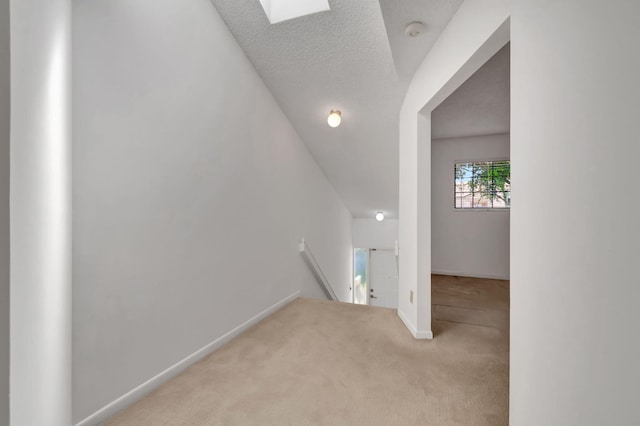 corridor with a textured ceiling, a skylight, and light colored carpet