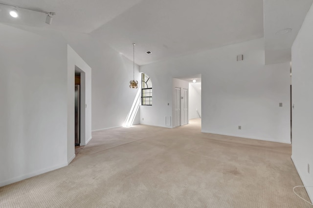 carpeted empty room with lofted ceiling and rail lighting