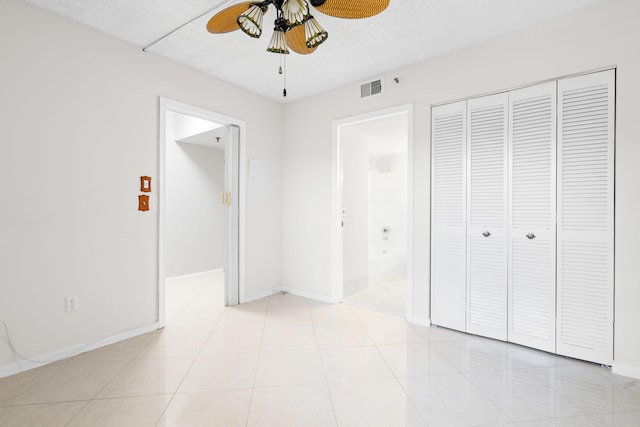 unfurnished bedroom featuring ceiling fan, light tile patterned flooring, a closet, and ensuite bathroom