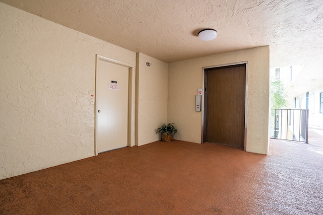 carpeted spare room featuring a textured ceiling and elevator