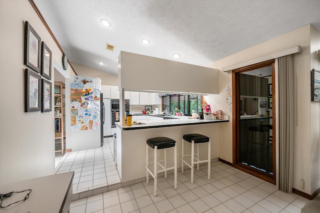 kitchen with a textured ceiling, lofted ceiling, kitchen peninsula, white cabinetry, and light tile patterned floors