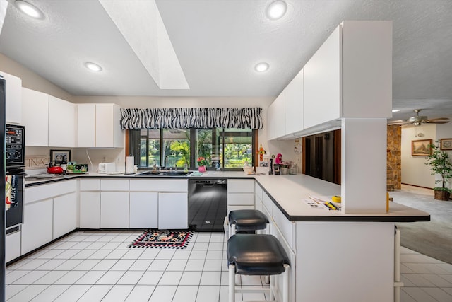 kitchen featuring kitchen peninsula, a textured ceiling, white cabinetry, black dishwasher, and a kitchen bar