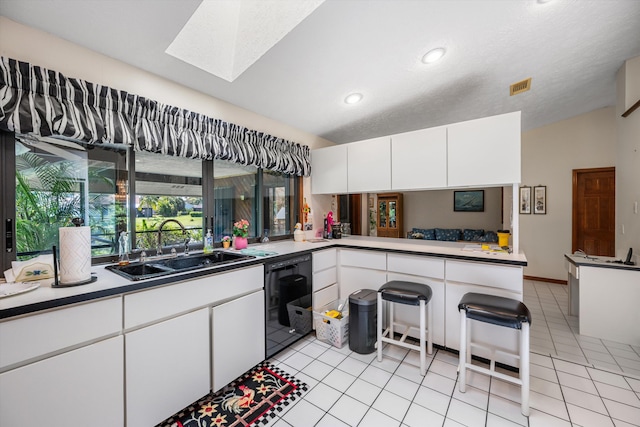 kitchen featuring white cabinets, kitchen peninsula, light tile patterned floors, vaulted ceiling with skylight, and sink