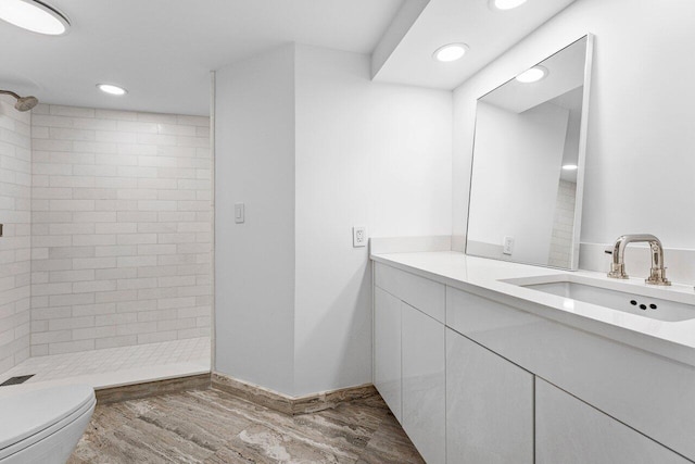 bathroom featuring toilet, hardwood / wood-style flooring, vanity, and tiled shower